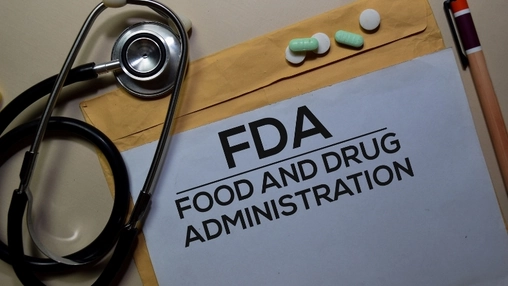 White document labelled FDA Food and Drug Administration with a stethoscope, pills, and pen on a desk