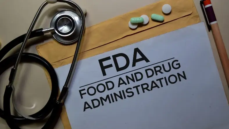 White document labelled FDA Food and Drug Administration with a stethoscope, pills, and pen on a desk
