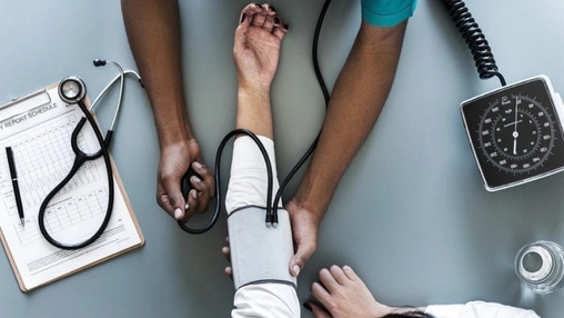 Overhead view of a clinician measuring blood pressure with stethoscope and report form visible on a clipboard