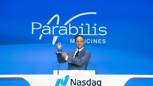 Man holding a commemorative glass at a Nasdaq podium beneath the Parabilis Medicines logo backdrop