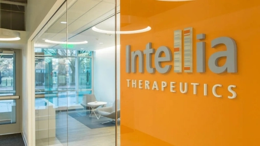 Intellia Therapeutics sign on an orange glass wall at a corporate entrance with a bright modern lobby beyond