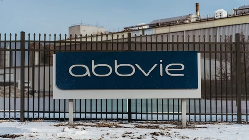 Exterior AbbVie sign in front of a metal security fence and industrial building during winter conditions