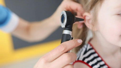 Close-up of a black otoscope being used to examine a child's ear by a healthcare professional in blue gloves
