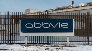 Exterior AbbVie sign in front of a metal security fence and industrial building during winter conditions